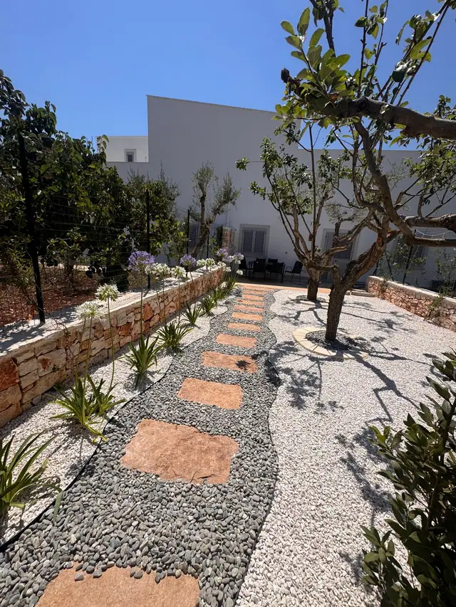 Sentiero in pietra e ghiaia tra agrumi e aiuole mediterranee in un giardino realizzato da Cesarino Giardini